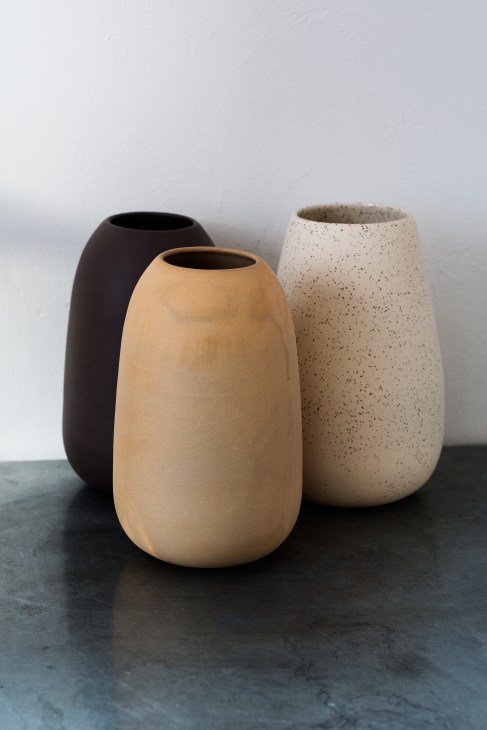 Three stoneware vessels in black, cream and speckled oat colors displaying simple functional forms.