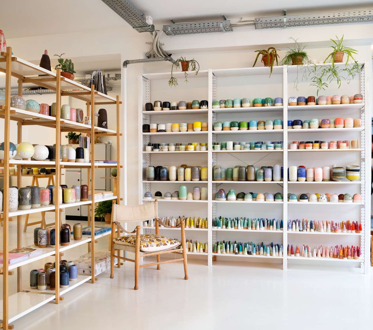 Studio Arhoj's bright shelving displays hundreds of colorful ceramic pots, glazes, and decorative vessels organized on wooden and white metal shelving units.