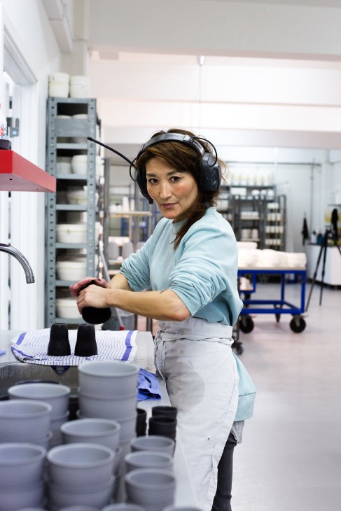 Potter wearing headphones works with clay vessels in a bright workshop studio.
