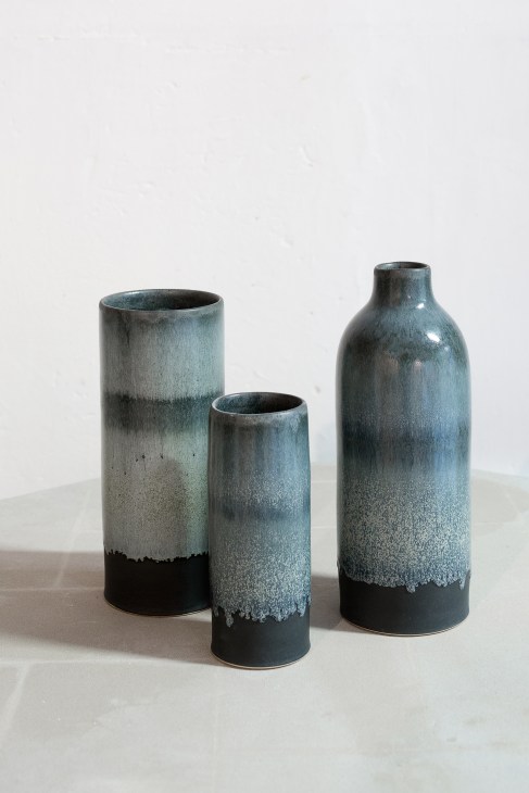 Three stoneware vessels with blue-grey cloudlike glaze fading to black bases arranged on white surface.