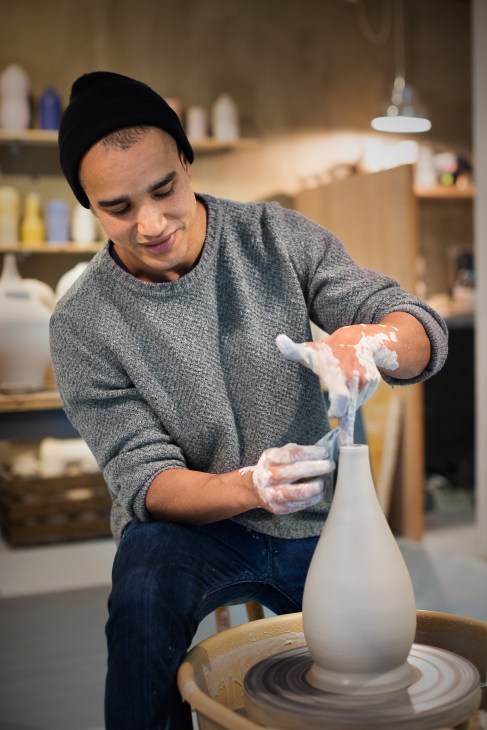 Potter Eric Landon shaping white stoneware clay on a rotating wheel in his studio.