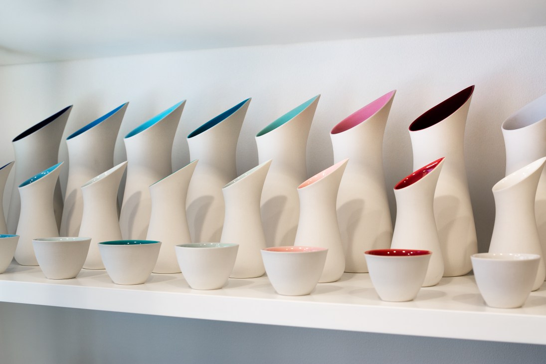 Display of white porcelain vessels with colorful glazed interiors in various shades of blue, pink, and red.