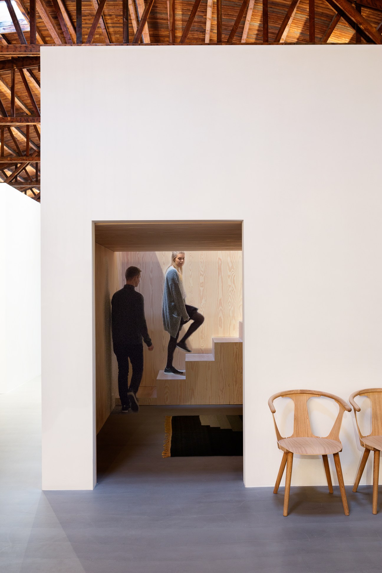 Interior of Dinesen House showroom with two people viewing wooden-lined alcove, wooden chairs by Sami Kallio visible in foreground.