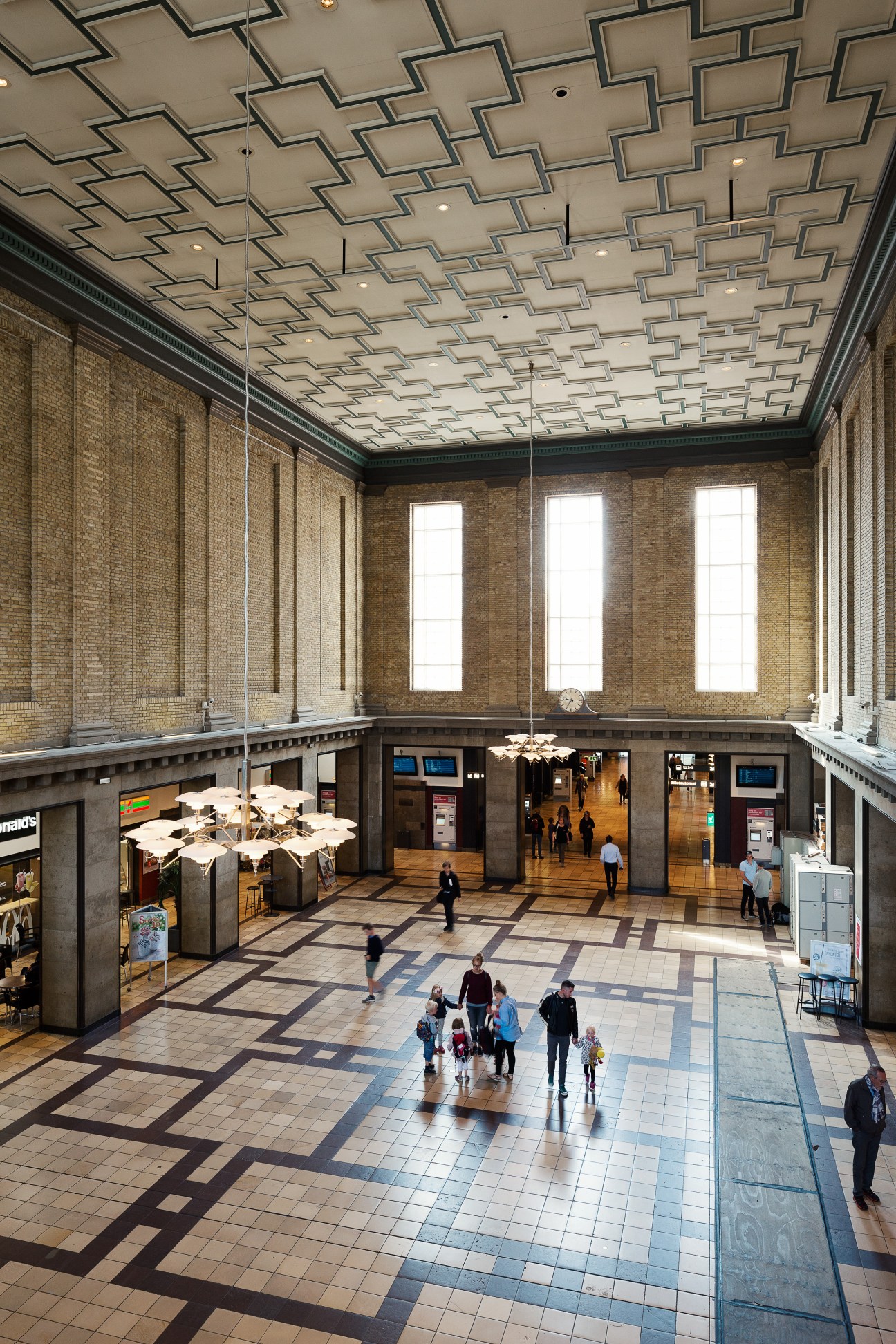 Interior of Aarhus Central Station featuring geometric patterned ceiling and brick walls with tall windows.