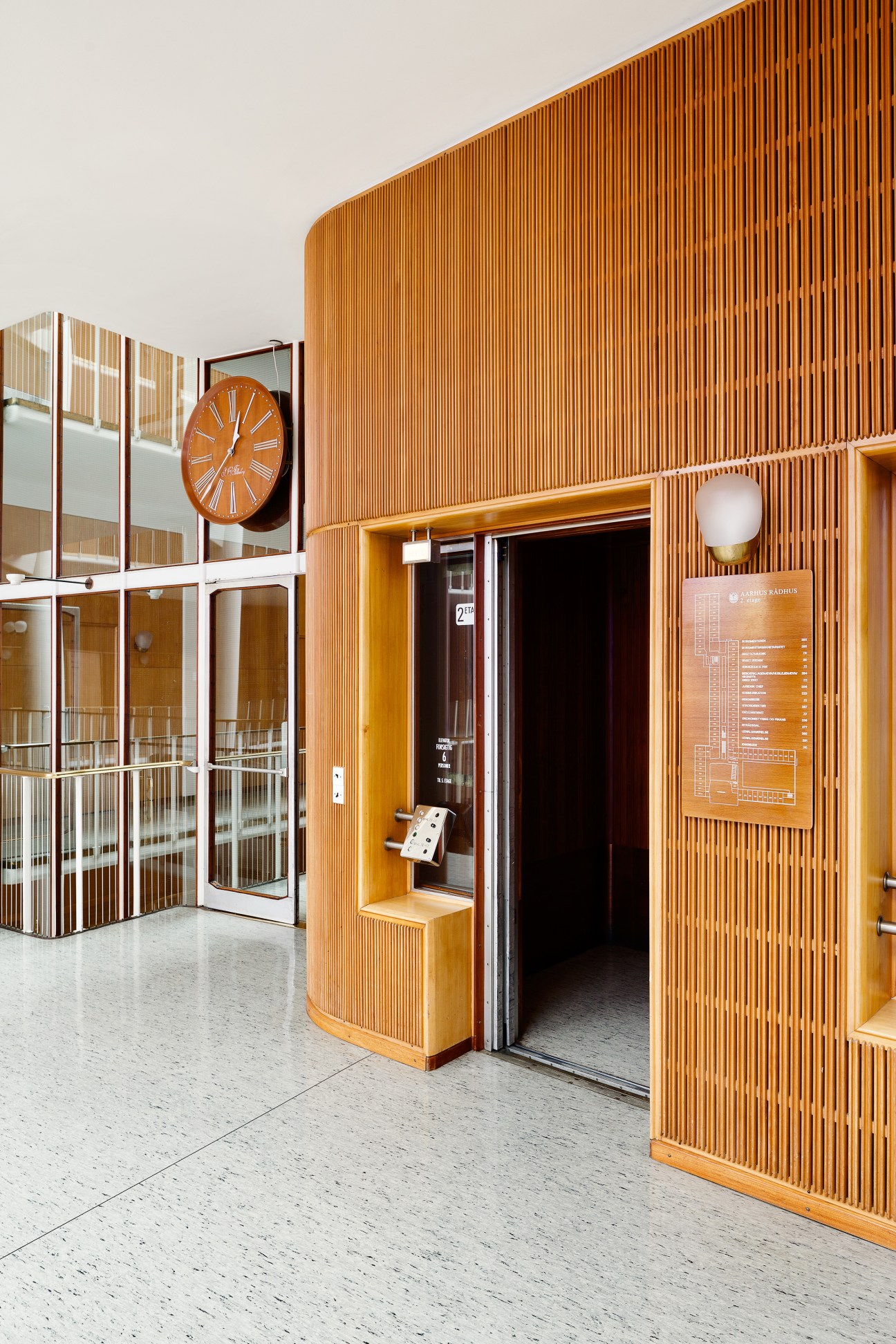 Interior of Aarhus city hall with wooden ribbed walls, orange clock, and modern fixtures.