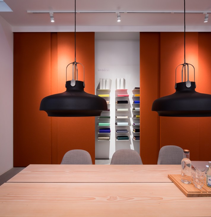 Kvadrat meeting room with black pendant lights, wooden table, grey chairs, and colorful fabric samples on shelving.