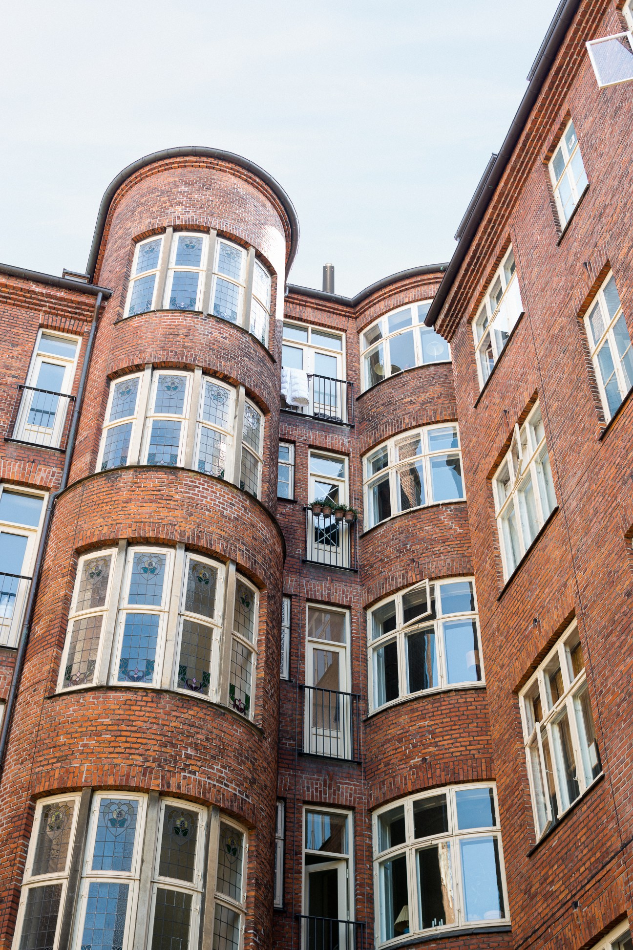 Red brick historic building facade with curved turret and large multi-pane windows viewed from courtyard.