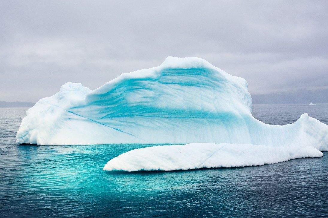 Turquoise and white icebergs floating in dark blue water under overcast sky.