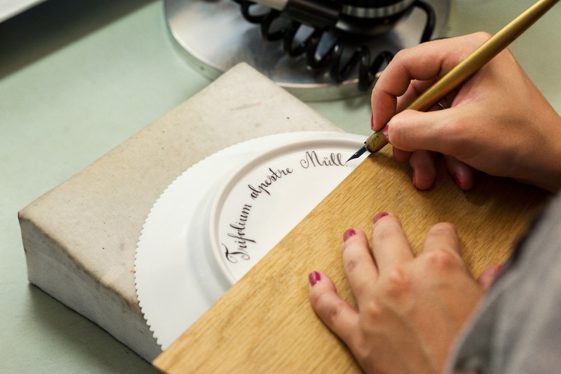 Hands writing plant name on back of white Royal Copenhagen porcelain plate with pen and ink.
