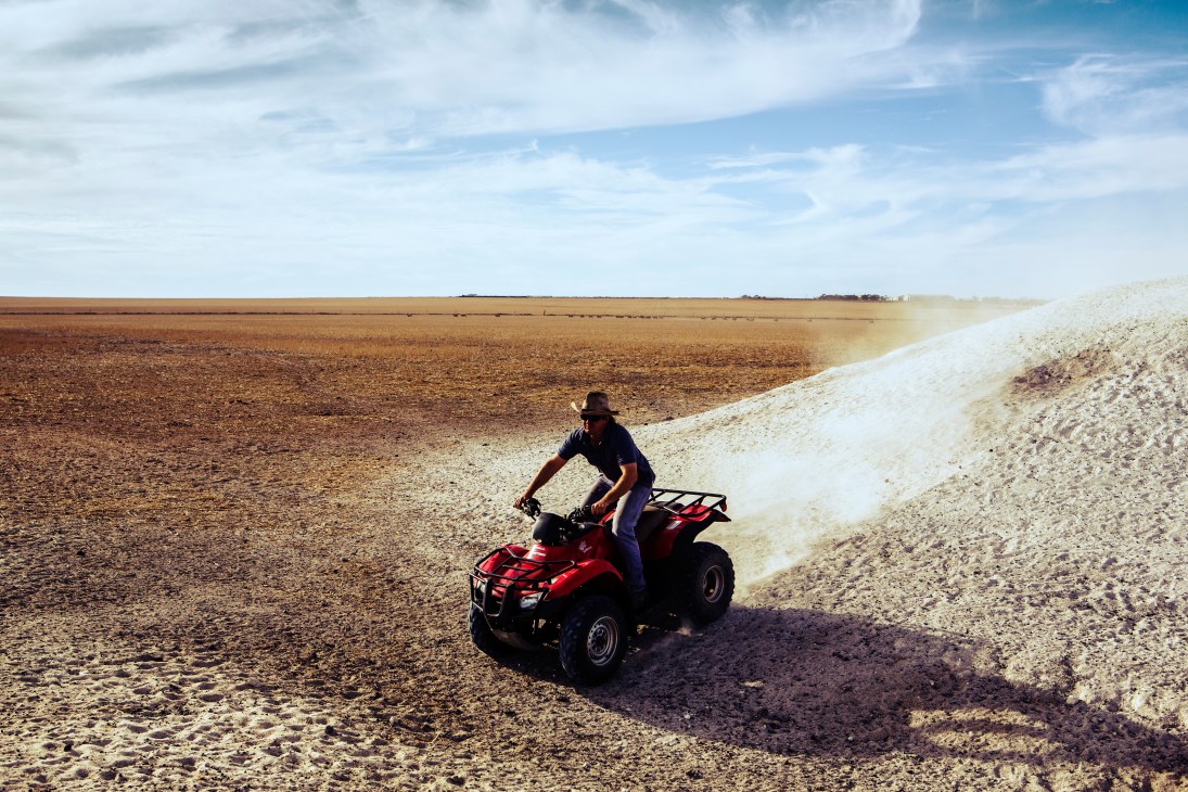 Farmer Leigh Spriggs rides a red quad bike across dusty farmland at Connemara in Western Australia's Wheatbelt.