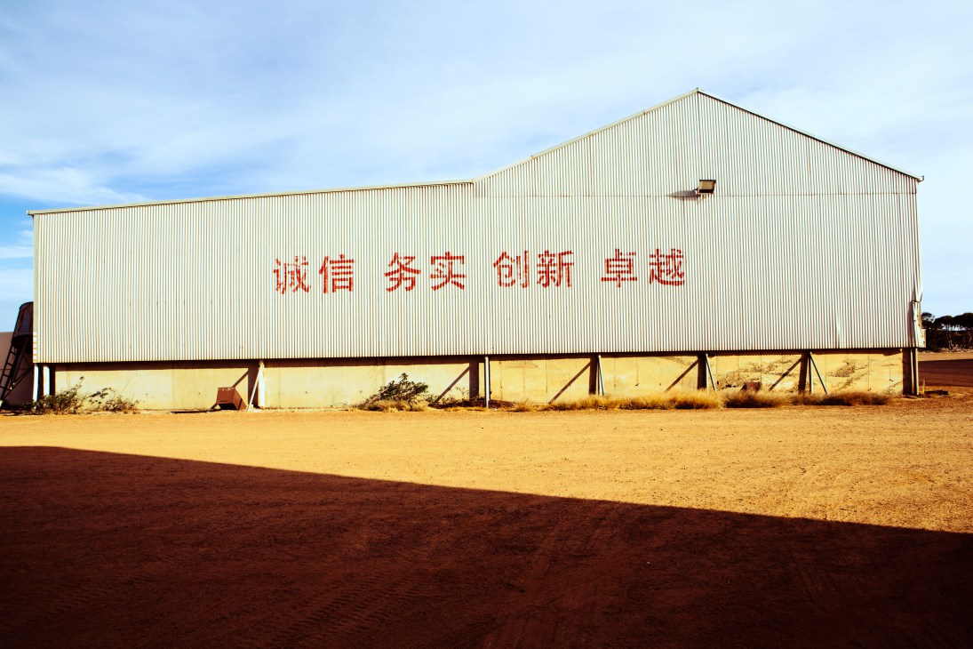 A large corrugated metal shed with Chinese characters spelling out Beidahuang Group's motto on a dirt farm.