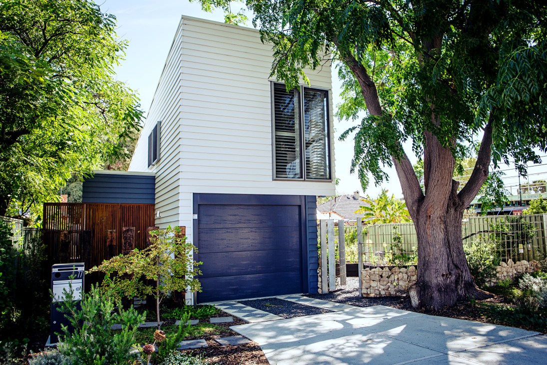 Modern white house with dark blue garage door surrounded by mature trees in Maylands, Perth.