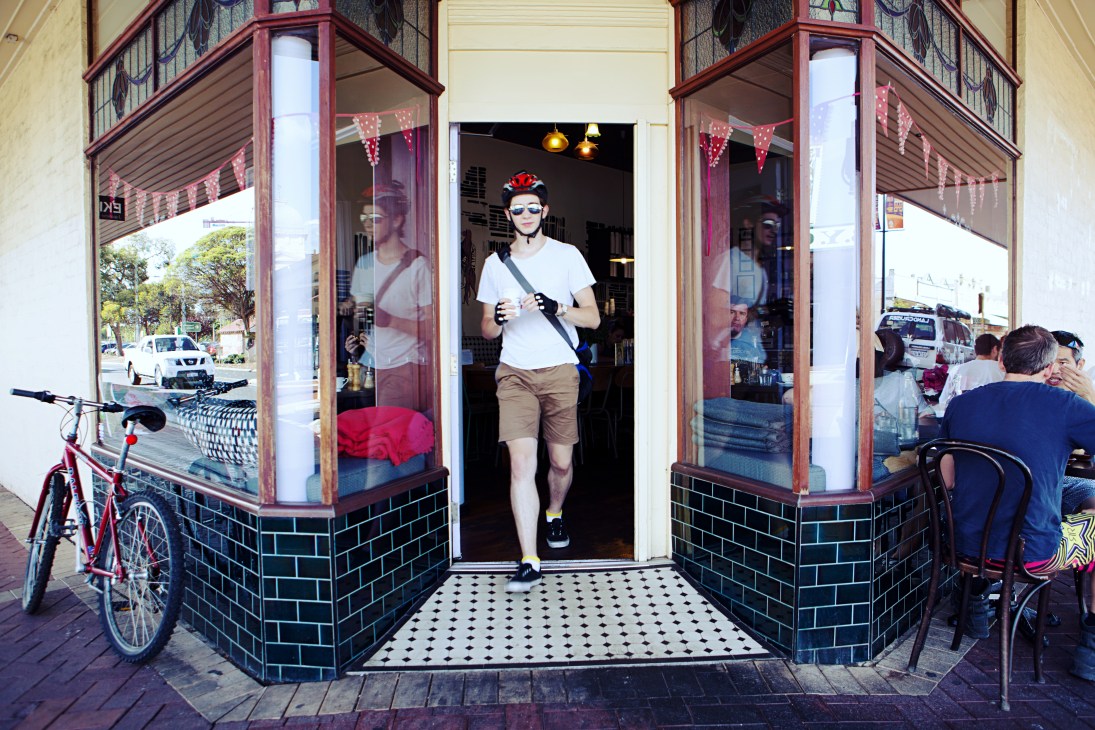 A jogger running past the storefront of Mrs S café in Maylands, Perth, with decorative bunting visible above.
