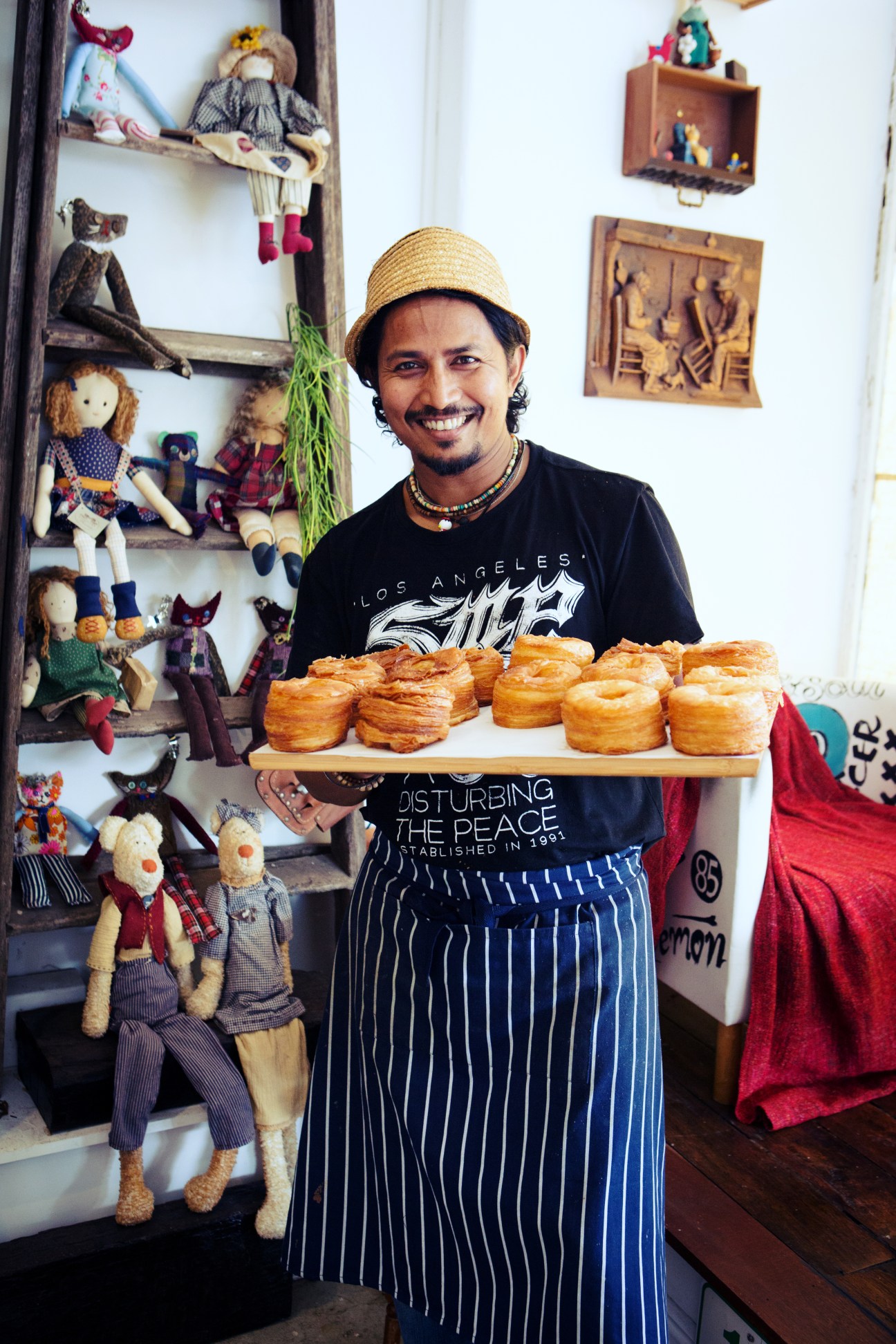 Man holding wooden board of pastries in front of shelves of handmade dolls at Nash & Co café.