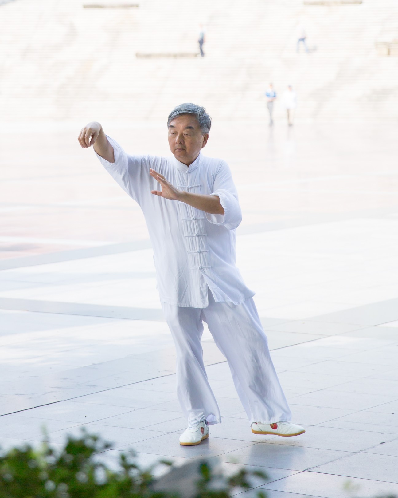 Man in white tai chi outfit performing tai chi in People's Square with buildings in background.