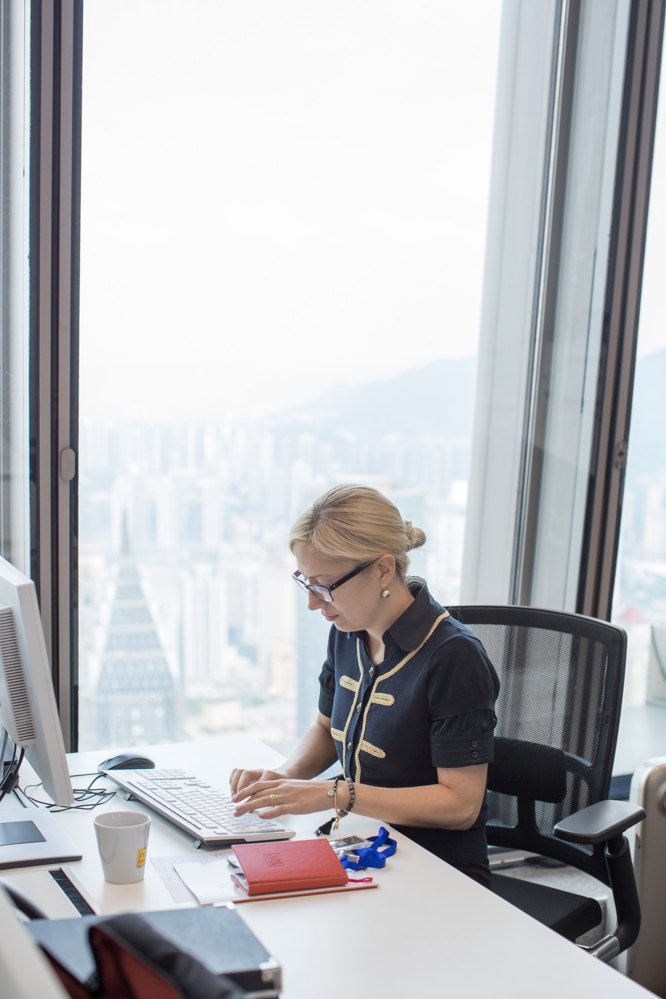 Rita Rozite, policy officer at the Dutch consulate, works at her desk with a city skyline visible through floor-to-ceiling windows behind her.