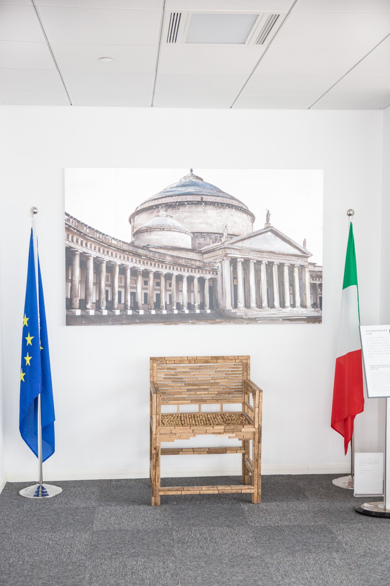 Interior of Italian consulate with EU and Italian flags flanking a classical architectural photograph.