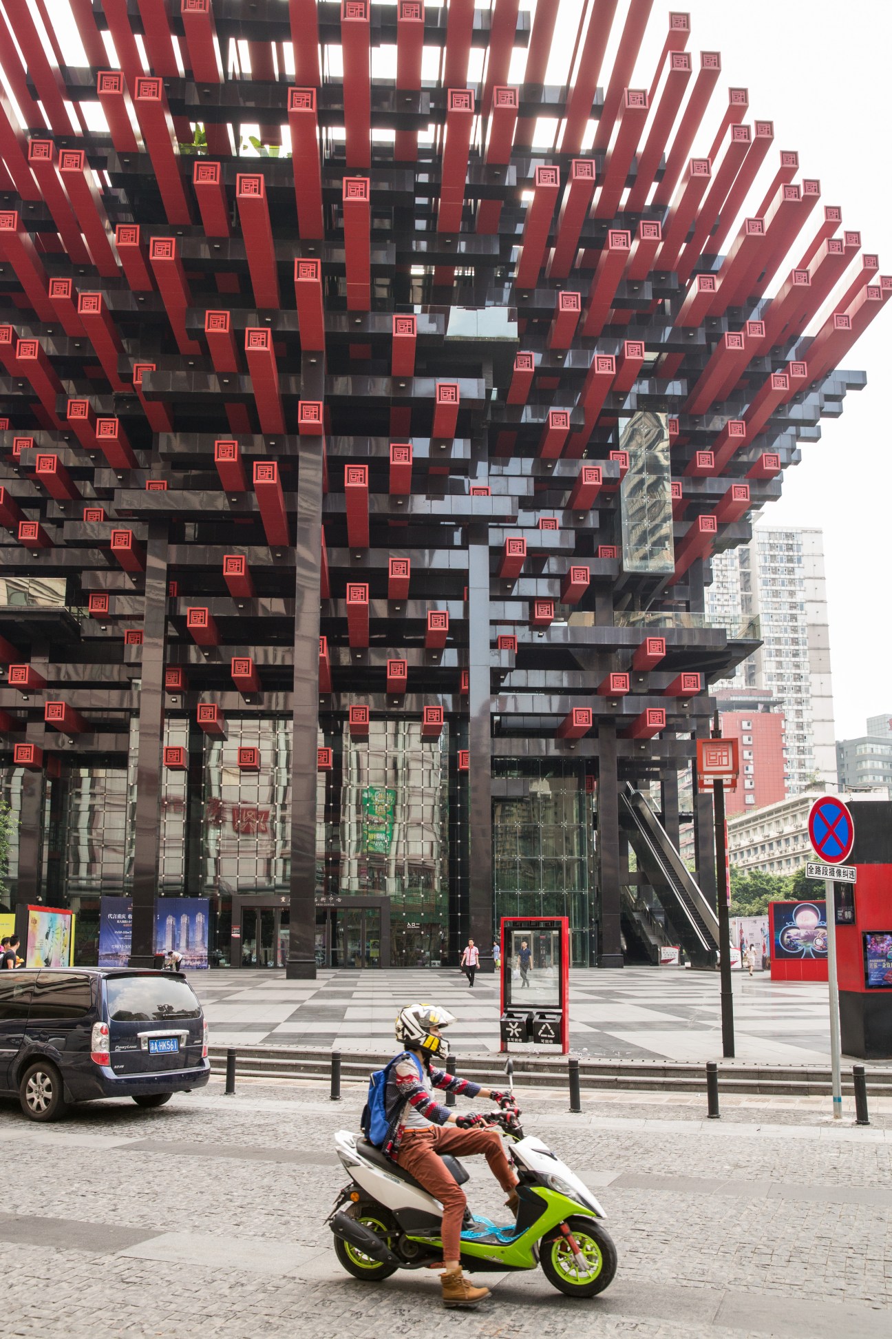 Scooter rider in front of Goutai Arts Centre's distinctive red latticed facade in Chongqing