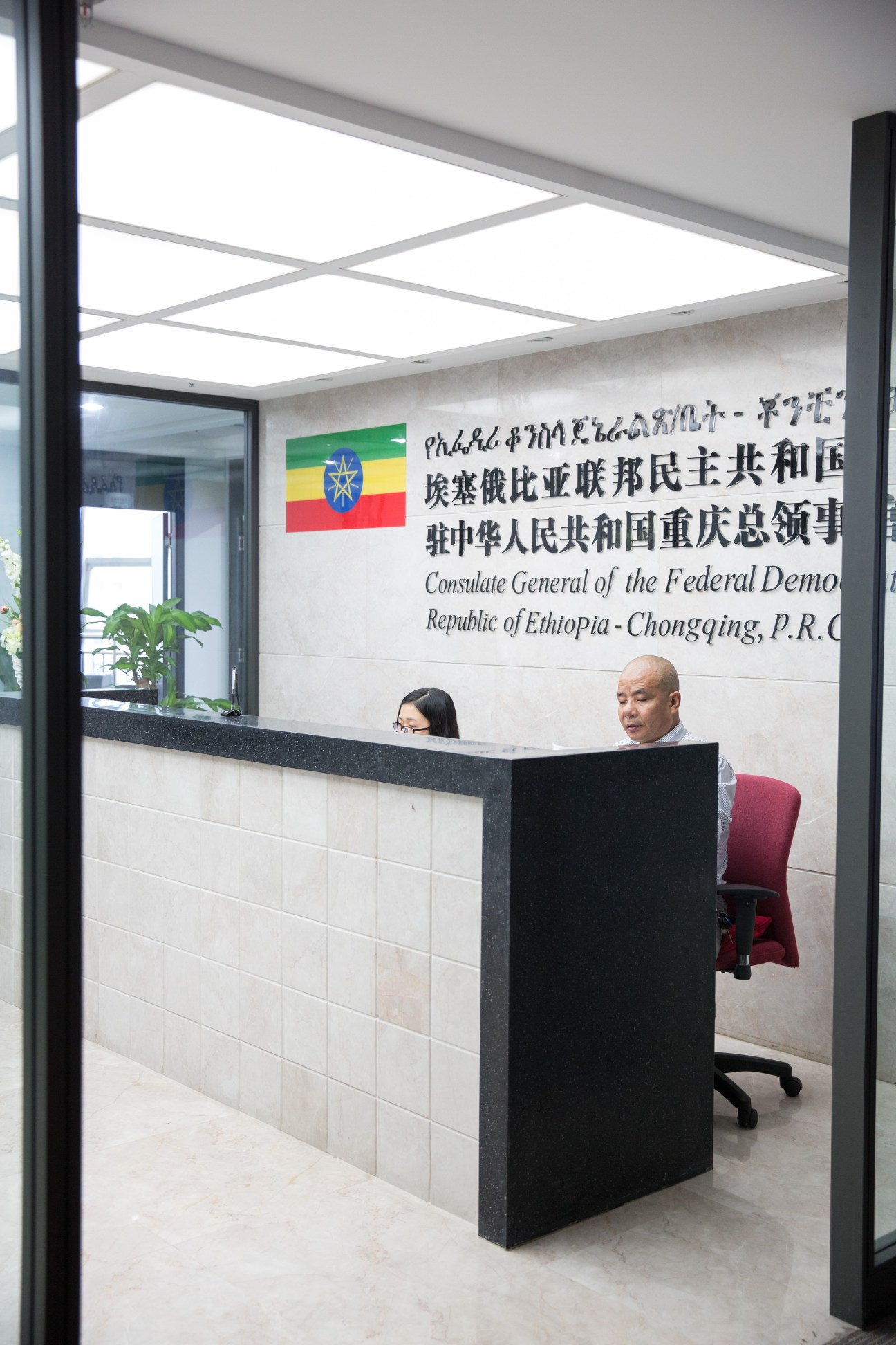 Interior of Ethiopia's consulate in Chongqing showing reception desk with staff and Ethiopian flag on wall.