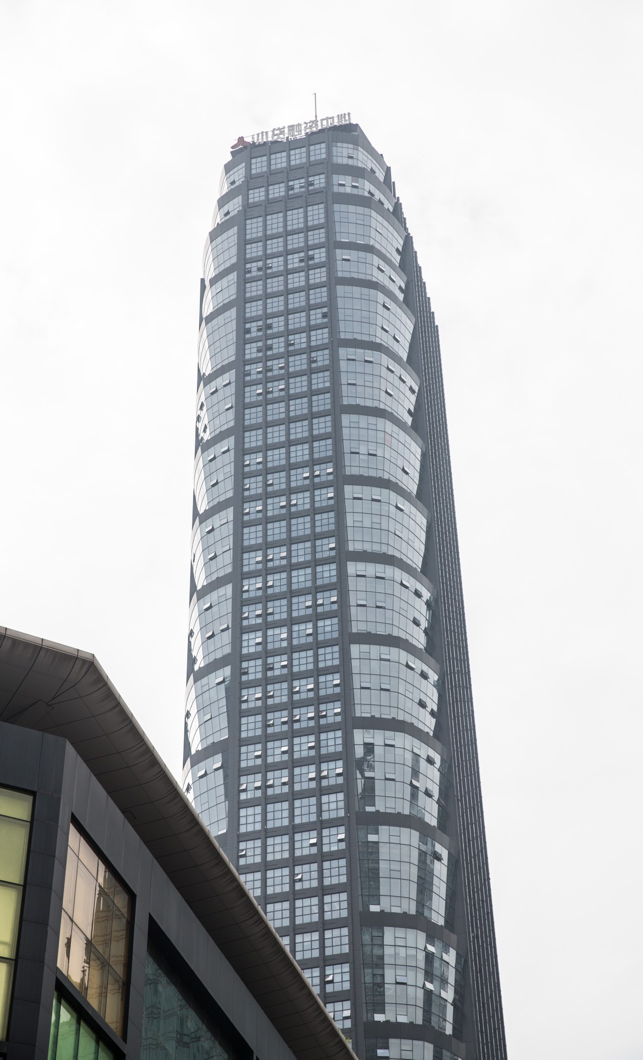 Tall cylindrical glass and steel tower building against overcast sky