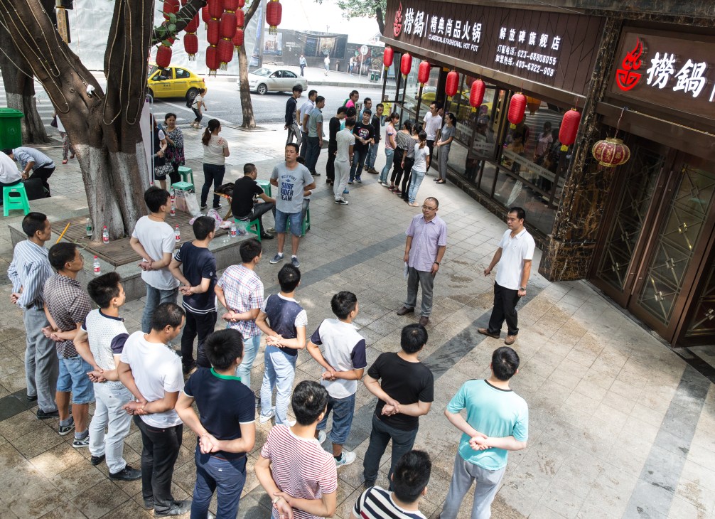 Restaurant staff lined up on a street outside a traditional Chinese restaurant with red lanterns and signage.