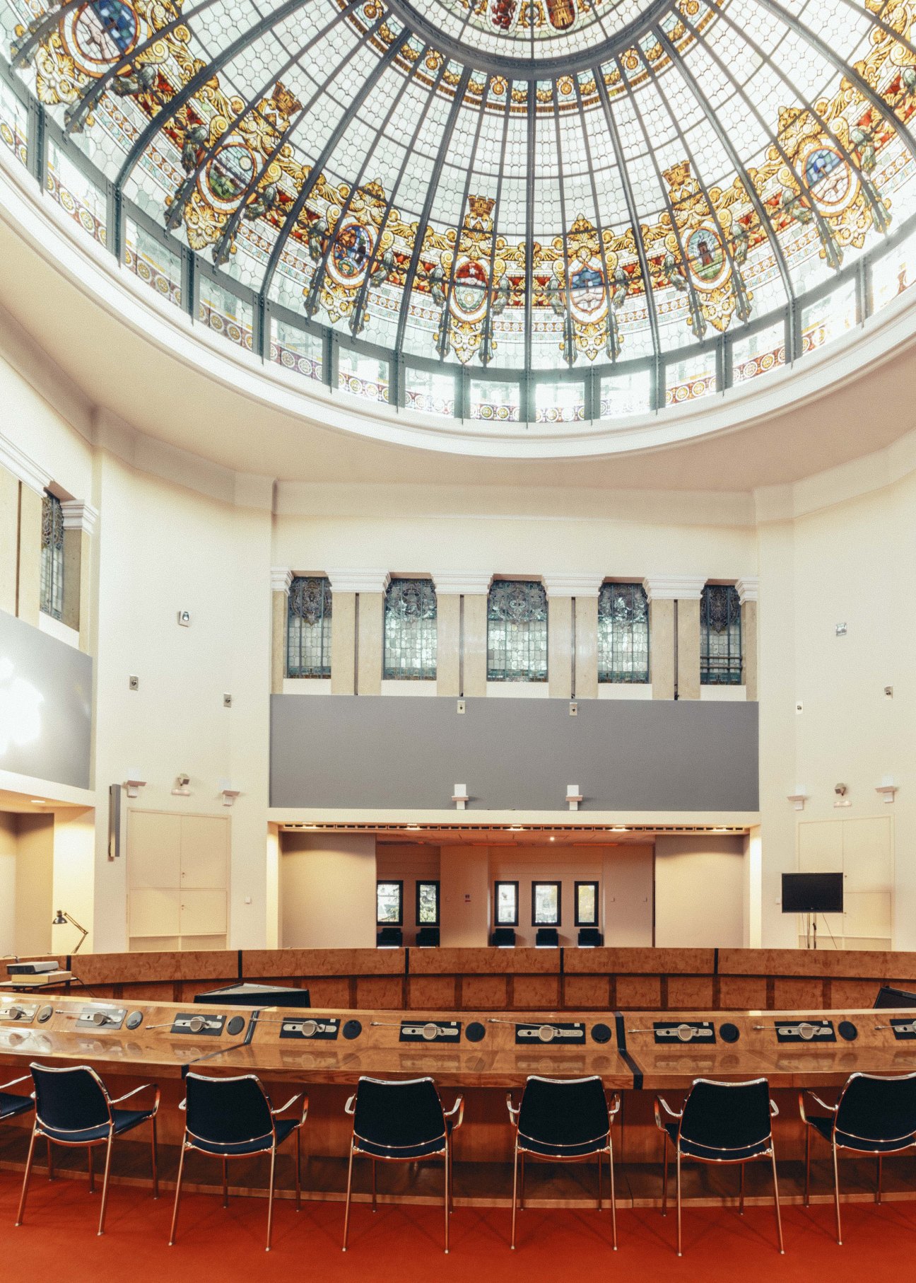 Interior of a grand roundtable discussion hall with ornate stained glass dome and modern seating.
