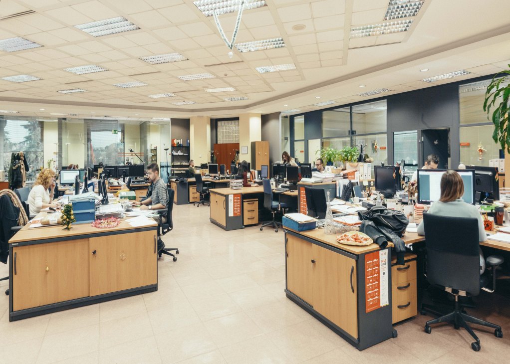 Open-plan office with multiple staff members working at desks with computers, studying Spanish language curriculum.