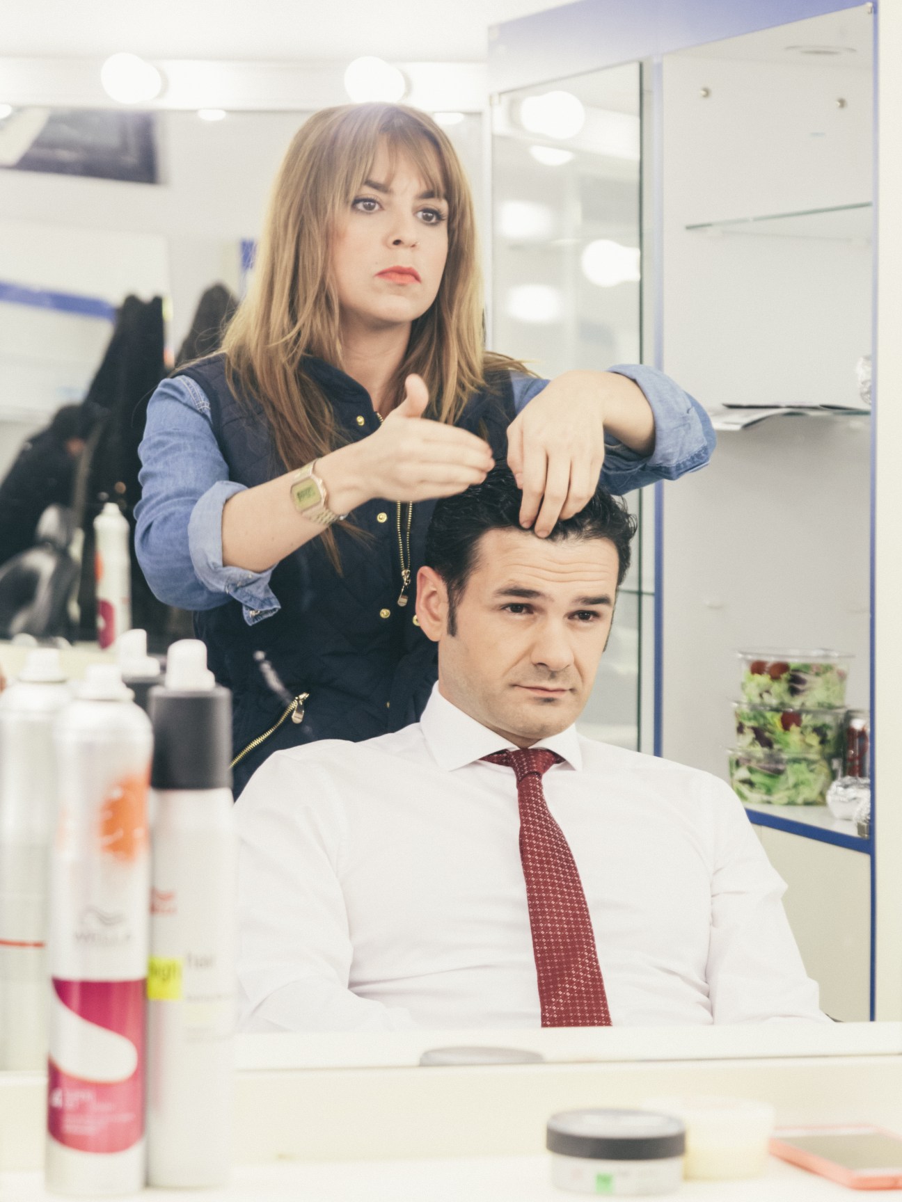 Host Iñaki López styling a guest's hair in a television studio dressing room.