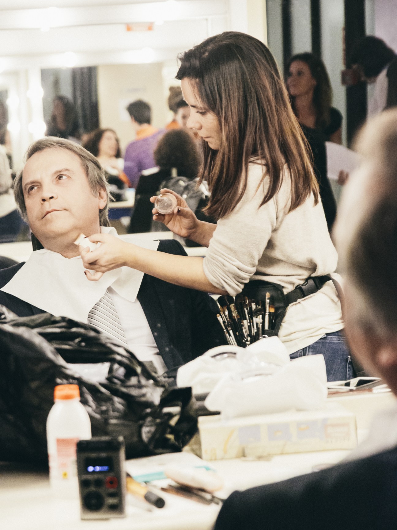 A makeup artist applies foundation to Antonio Miguel Carmona's face in a bright studio setting.