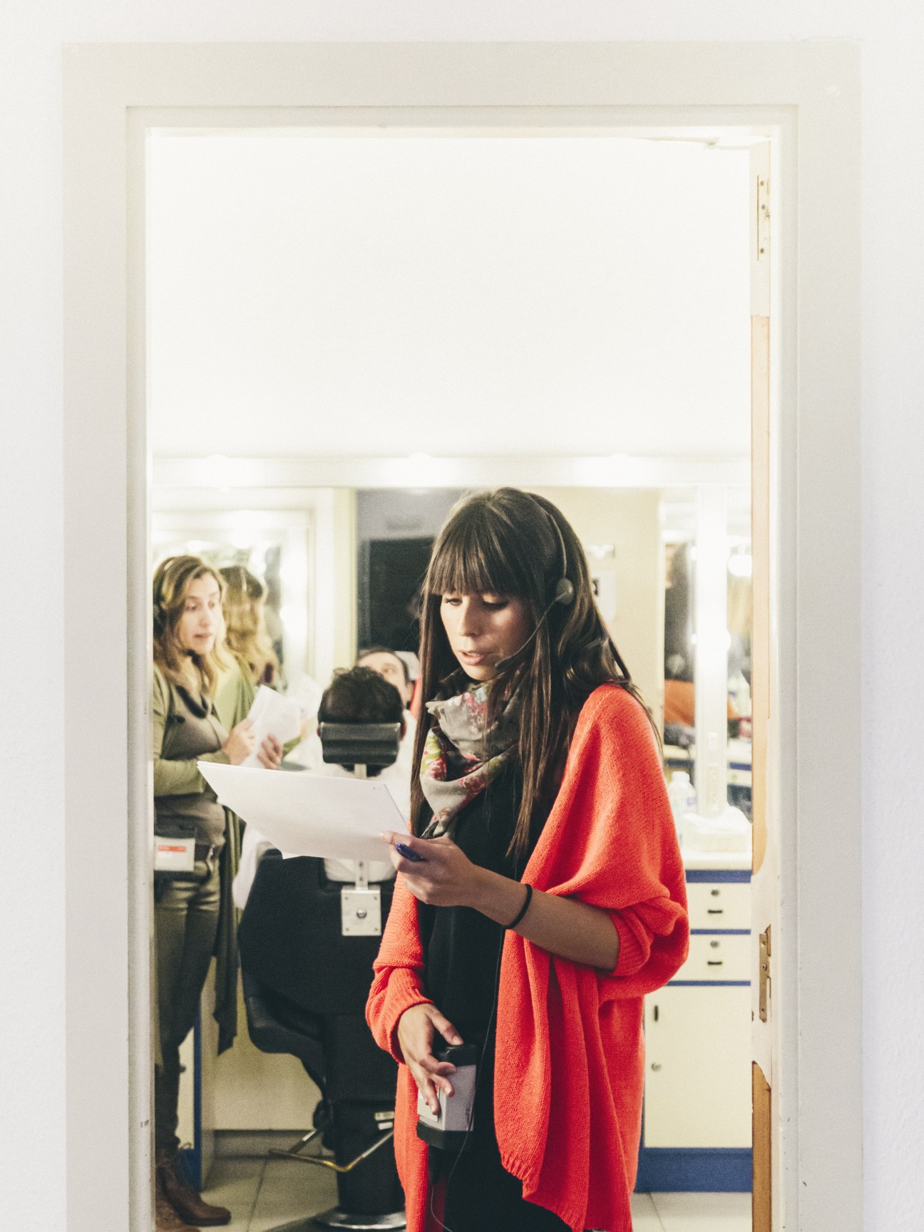 Carolina Quesada, guest booker for La Sexta Noche, holding papers in a studio hallway wearing a bright red cardigan.