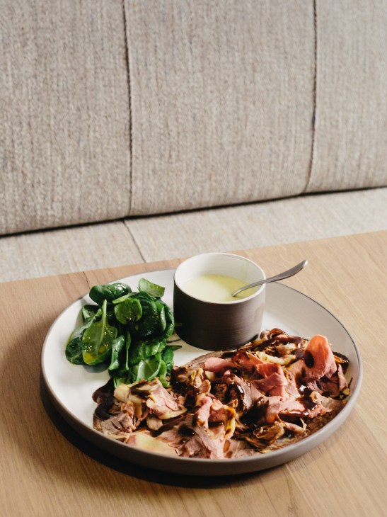 Roast loin of beef with mashed potatoes and spinach salad served on a white plate with sauce.