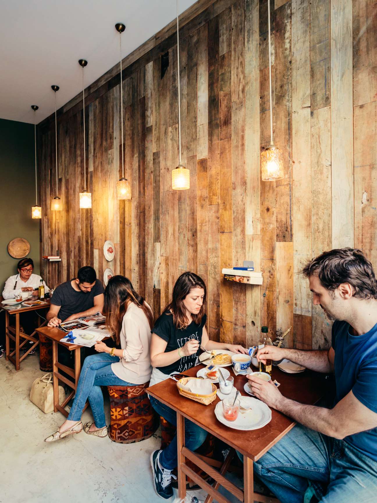 Customers dining at wooden tables in a café with reclaimed wood wall paneling and pendant lighting.