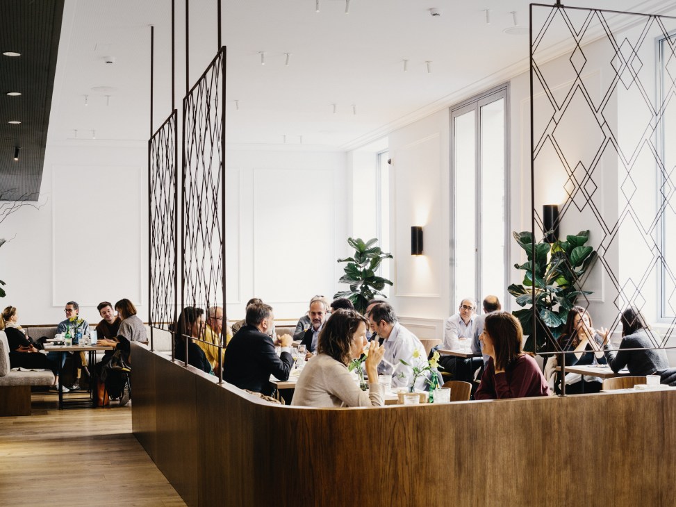 Interior of Hermosos & Malditos restaurant in Madrid with diners seated at tables and modern geometric wall panels.
