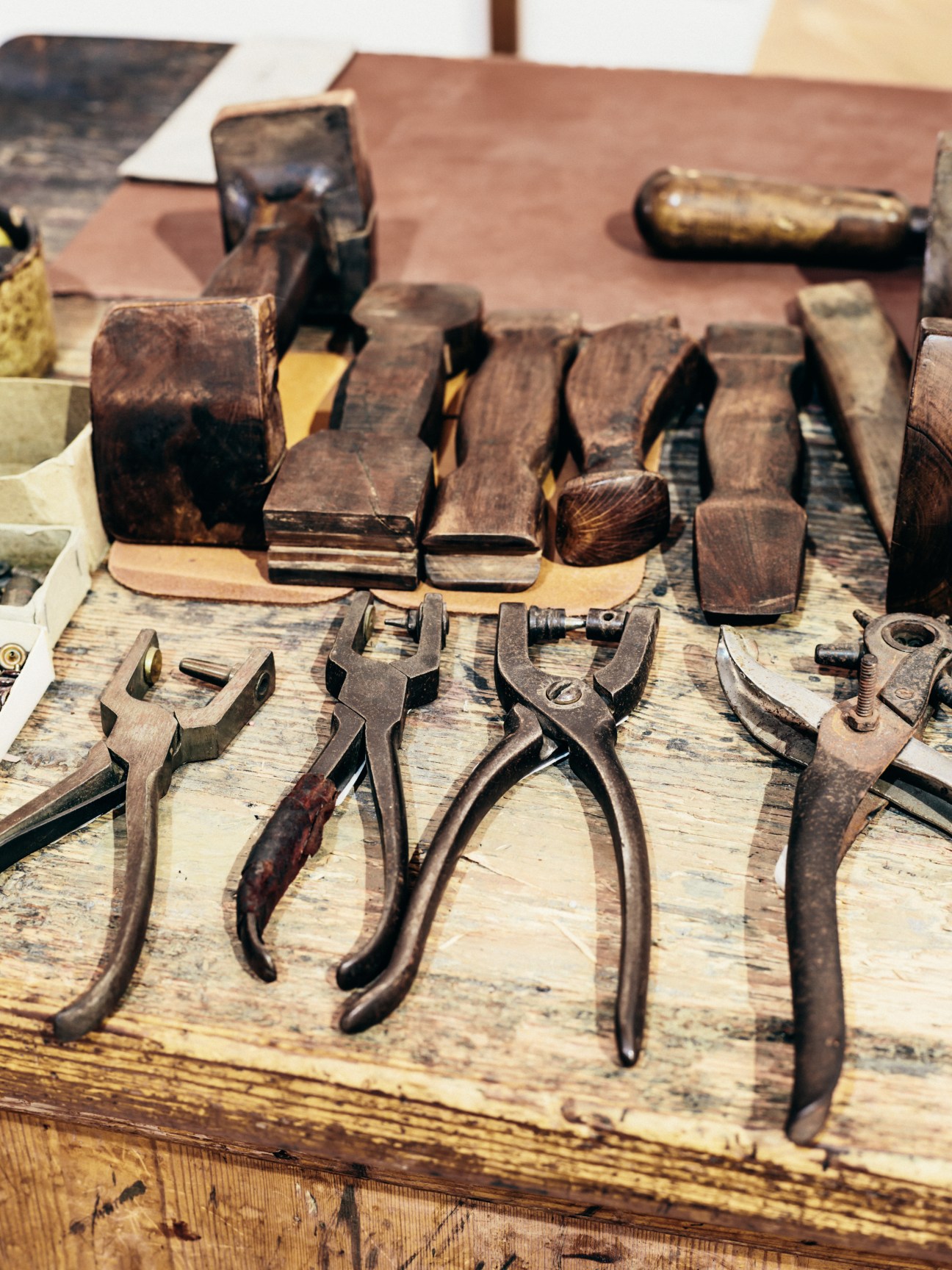 Antique leather-working tools including pliers, stamps, and cutting implements arranged on a wooden workbench.