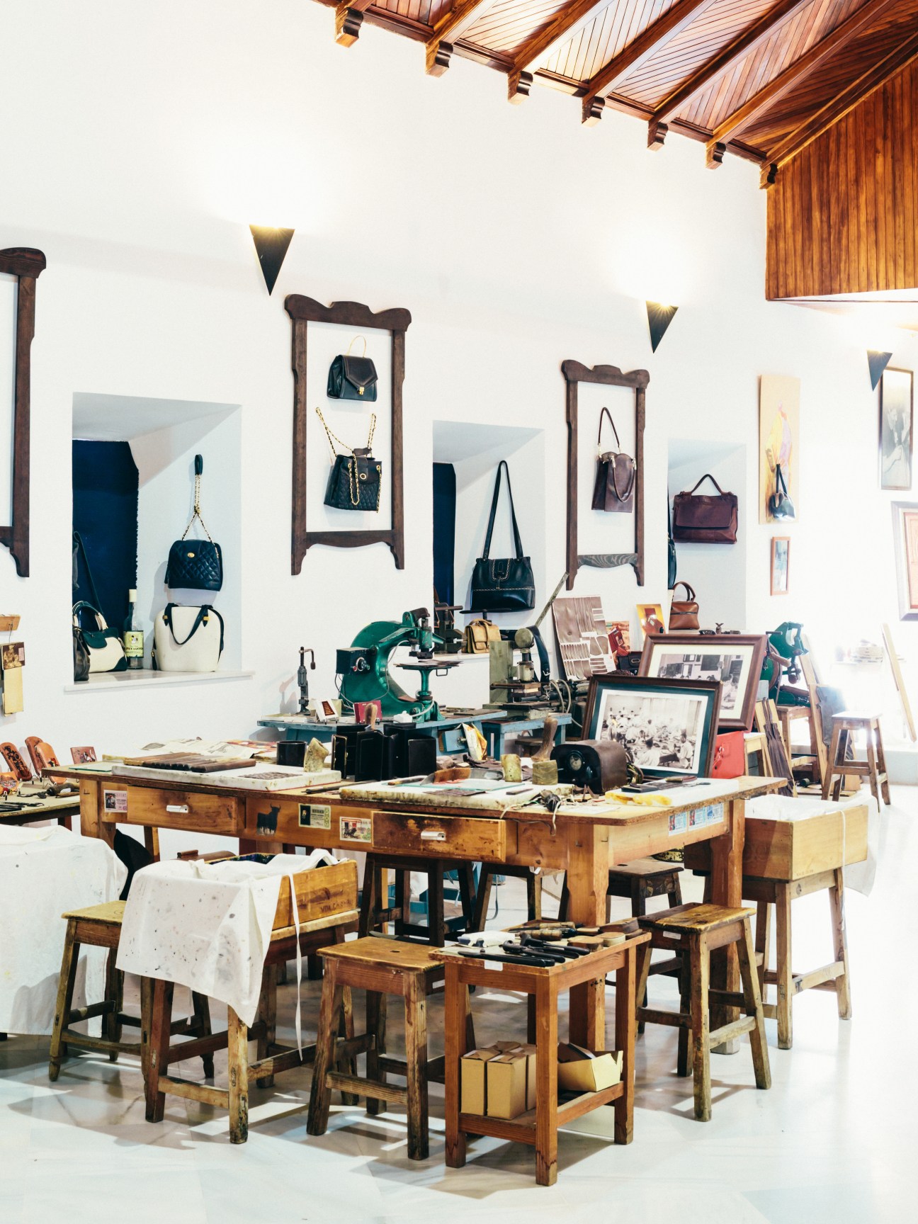 Museum display of leather handbags mounted on wooden frames above a workbench with tools and craft materials.