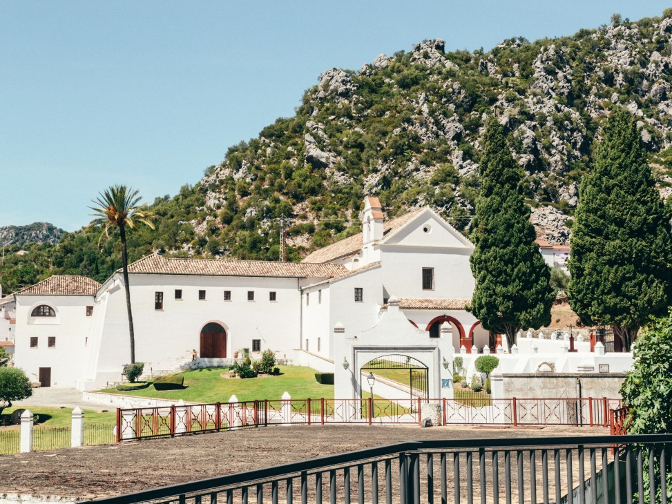 A white 17th-century Capuchinos convent with terracotta roof tiles nestled against rocky mountains in Ubrique, Spain.