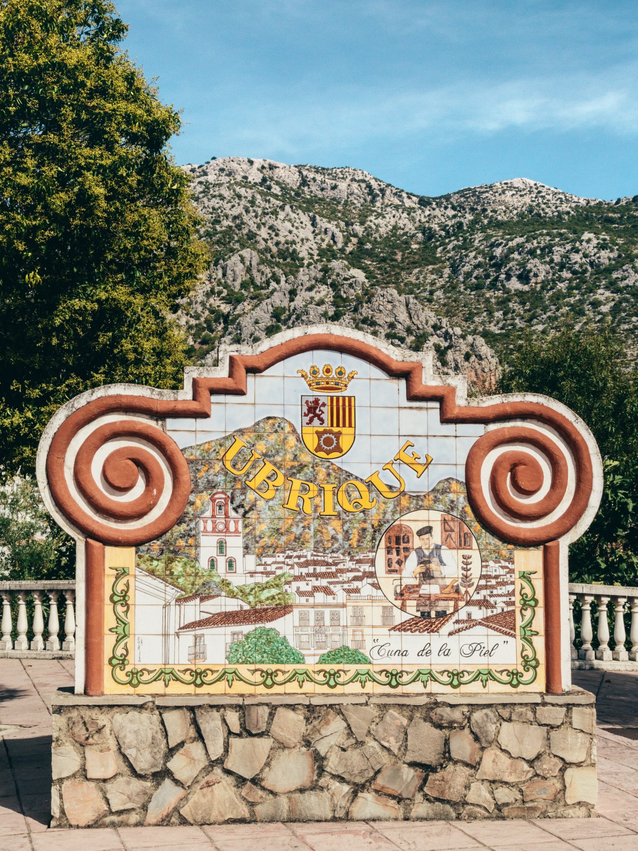 Ornate ceramic welcome sign for Ubrique with Spanish coat of arms and mountain backdrop.