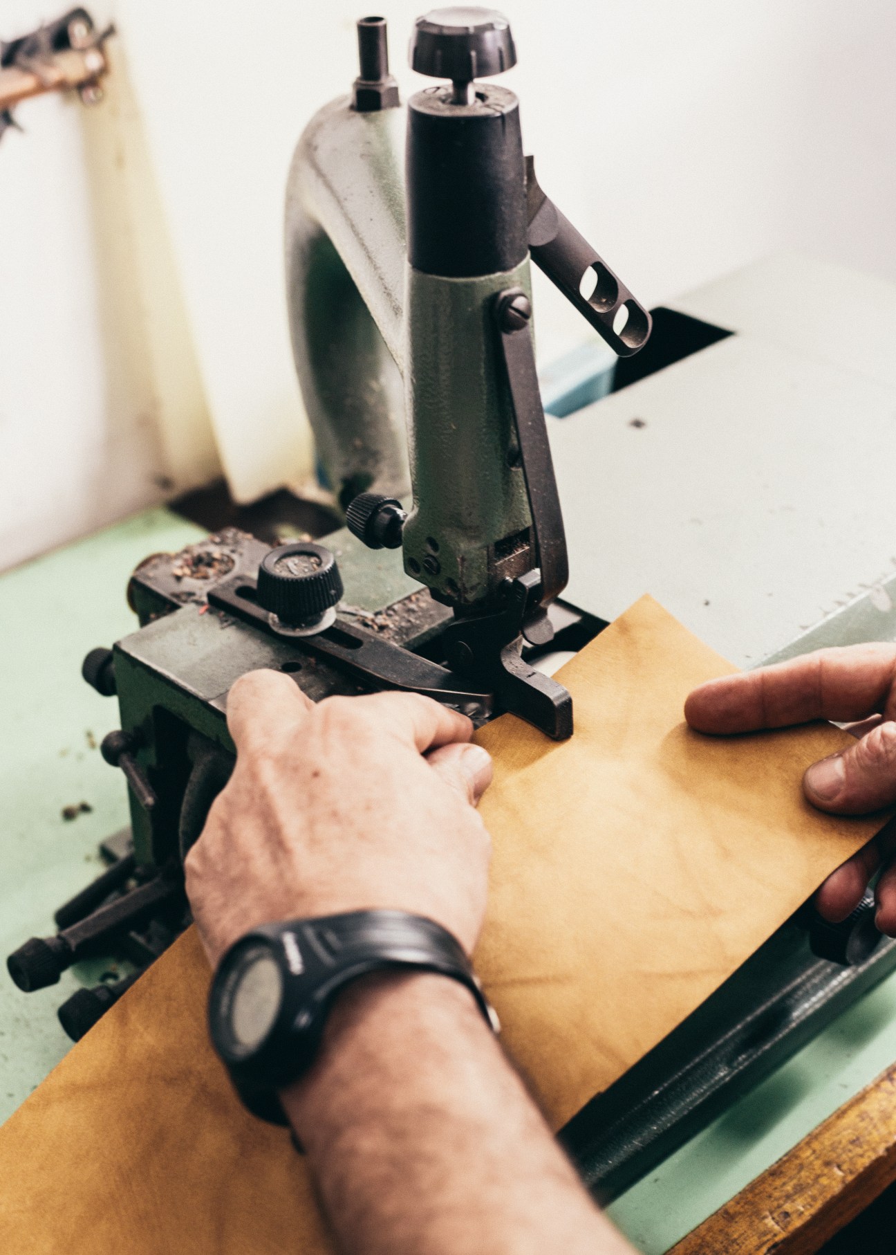 Artisan's hands operating a leather stamping press on tan leather material in a workshop.