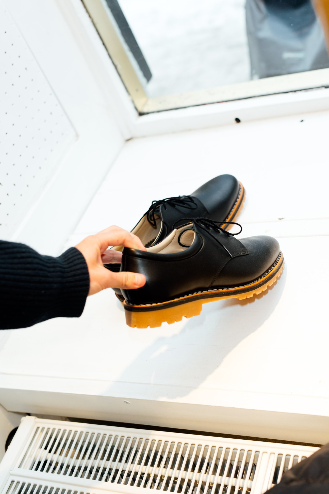 A person holding a black derby shoe with a yellow sole and tan leather trim.