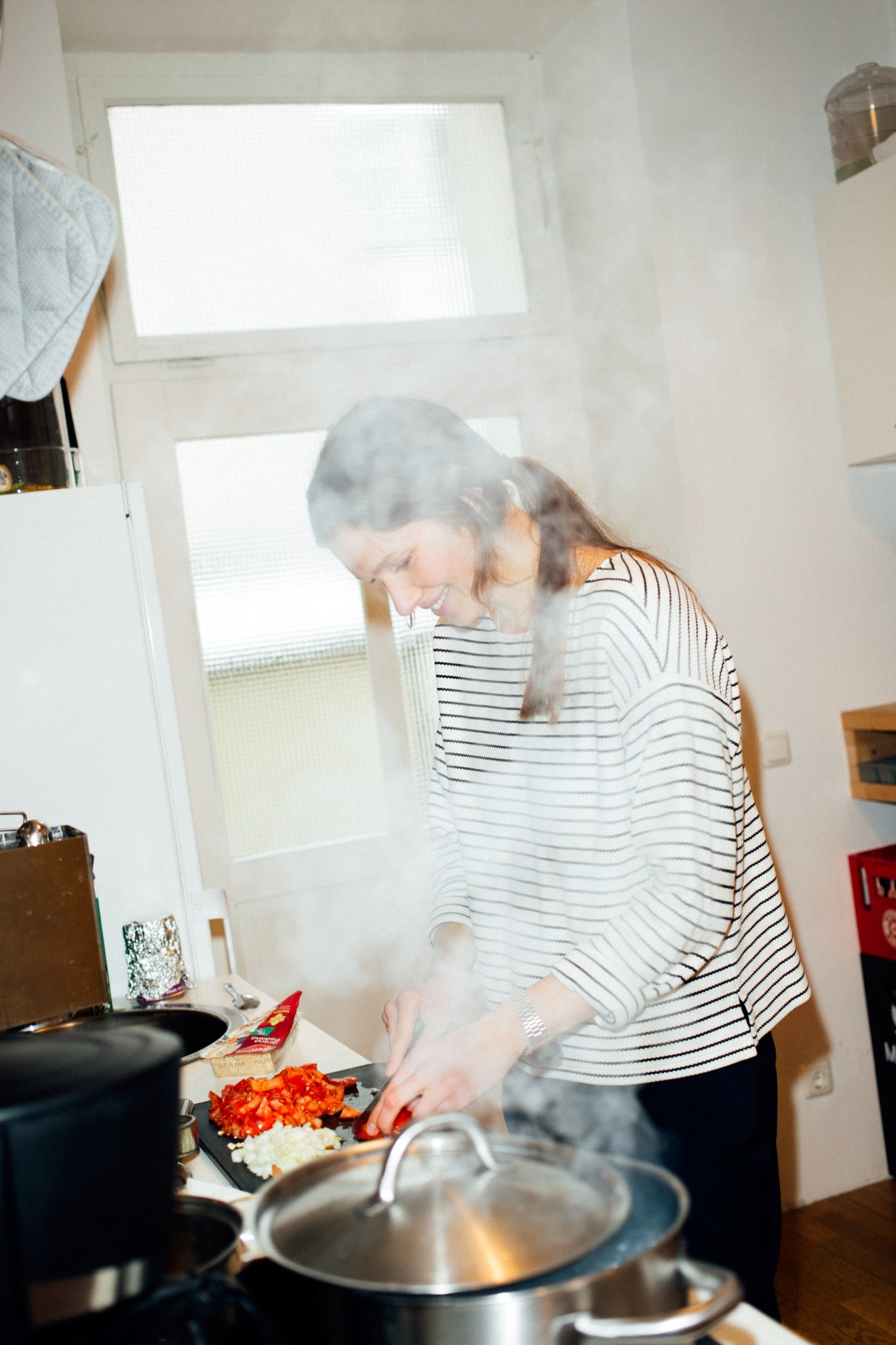Woman in striped shirt chopping red peppers in a kitchen while cooking lunch.