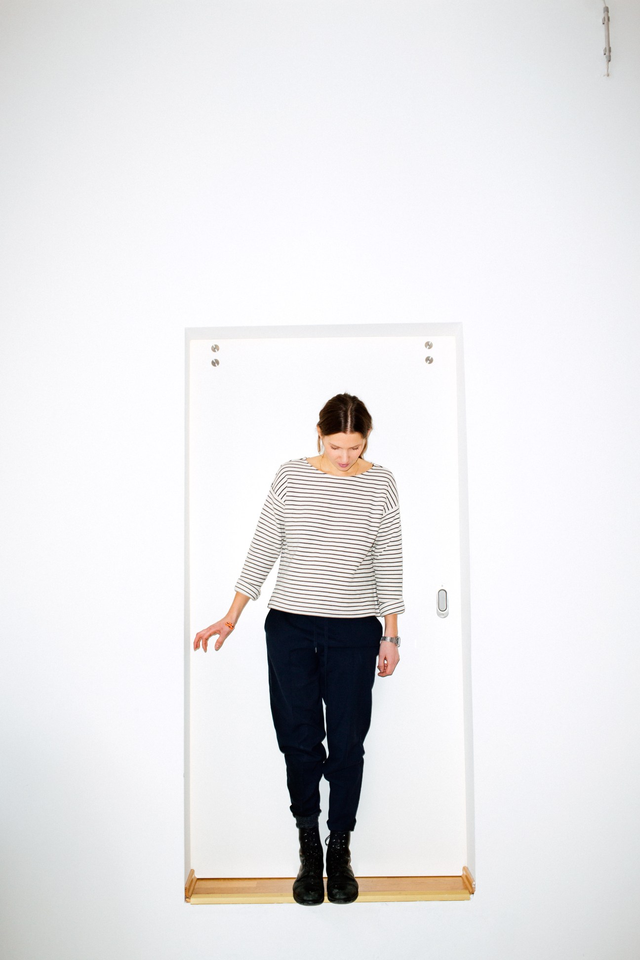Woman in striped shirt and dark pants standing in a white doorway frame.