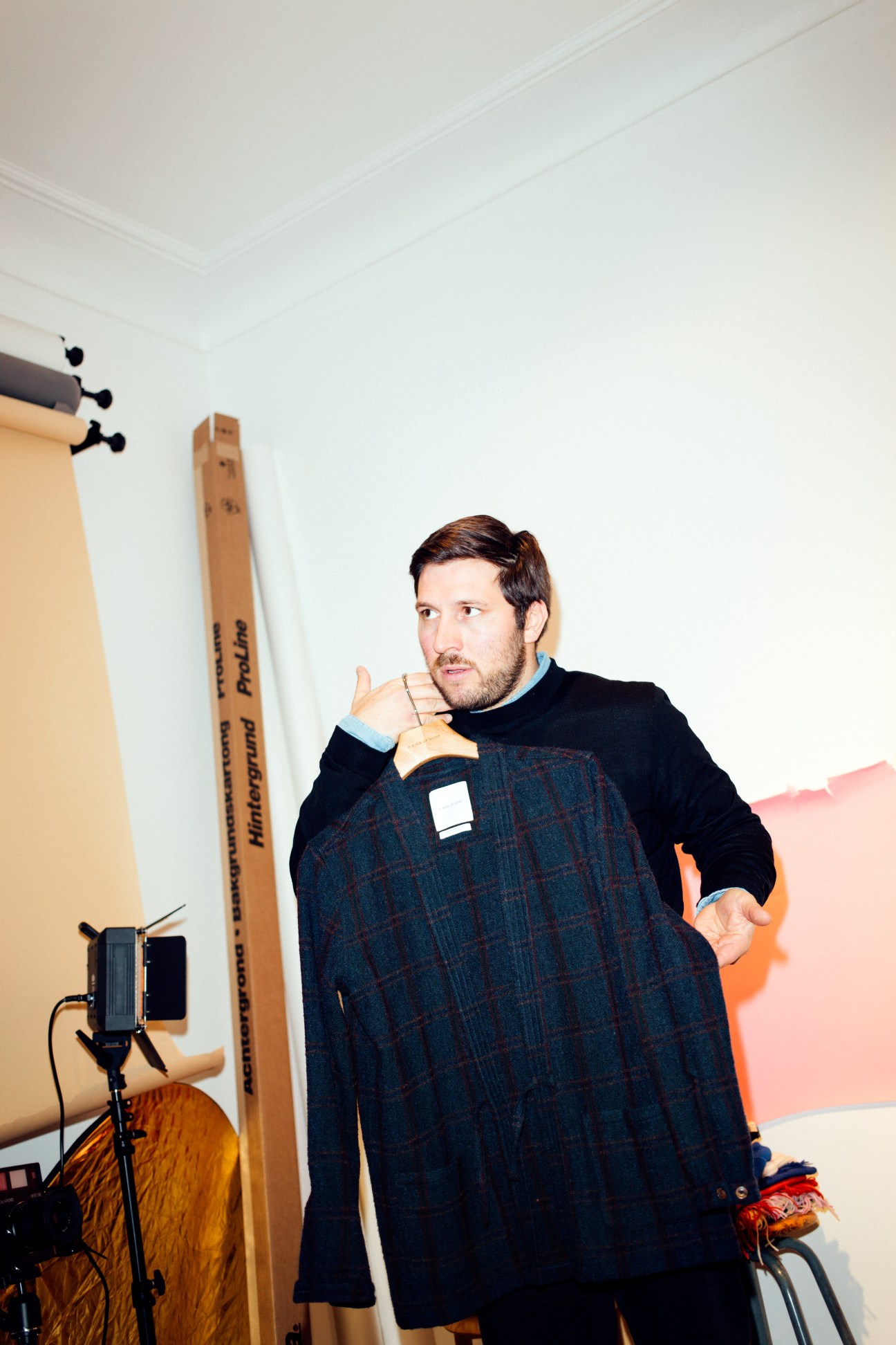 Yasar Ceviker holds up a dark plaid coat with black lining in A Kind of Guise's Munich studio.