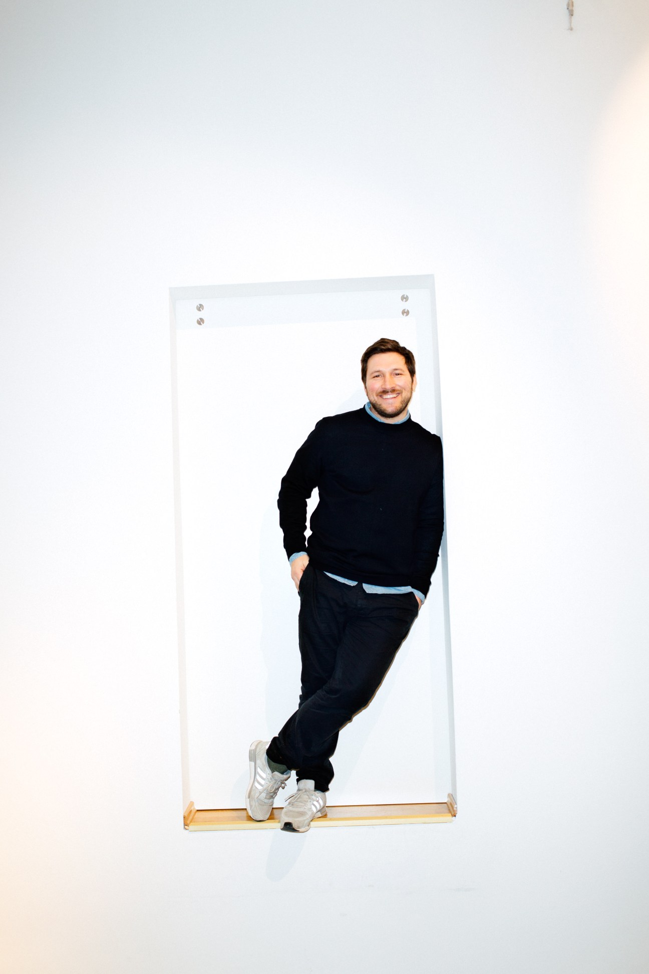 Yasar Ceviker, A Kind of Guise co-founder, leaning against a white panel wearing black clothing.