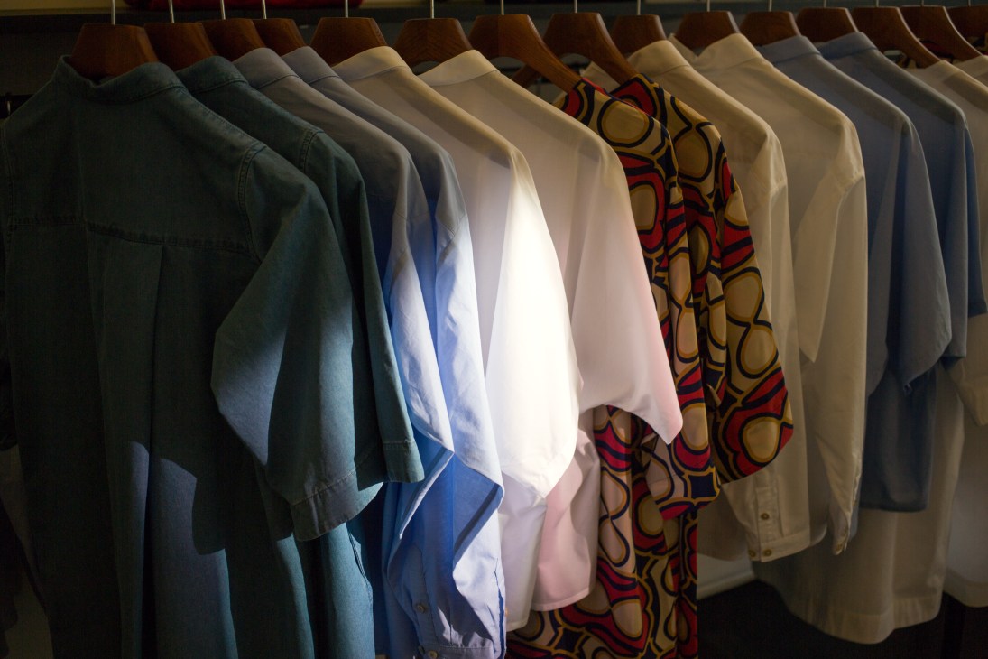 Clothing collection hanging on wooden hangers showing various neutral and patterned garments.