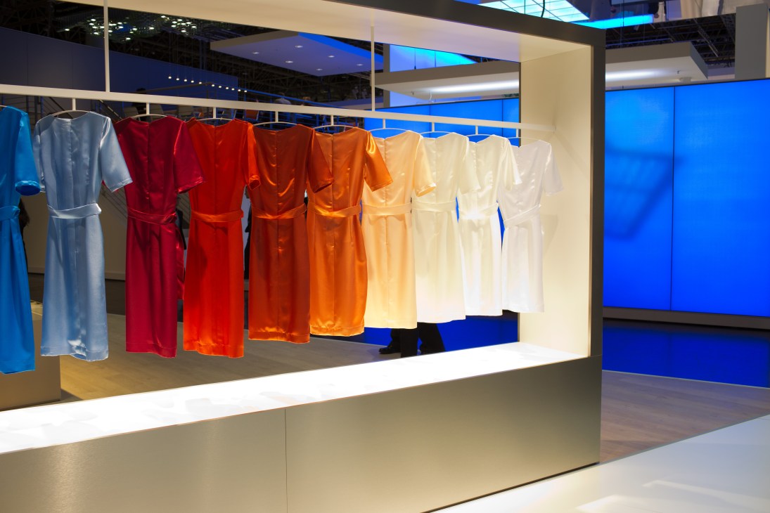 Minimalist retail display with colored dresses on hangers under bright LED lighting against blue walls.