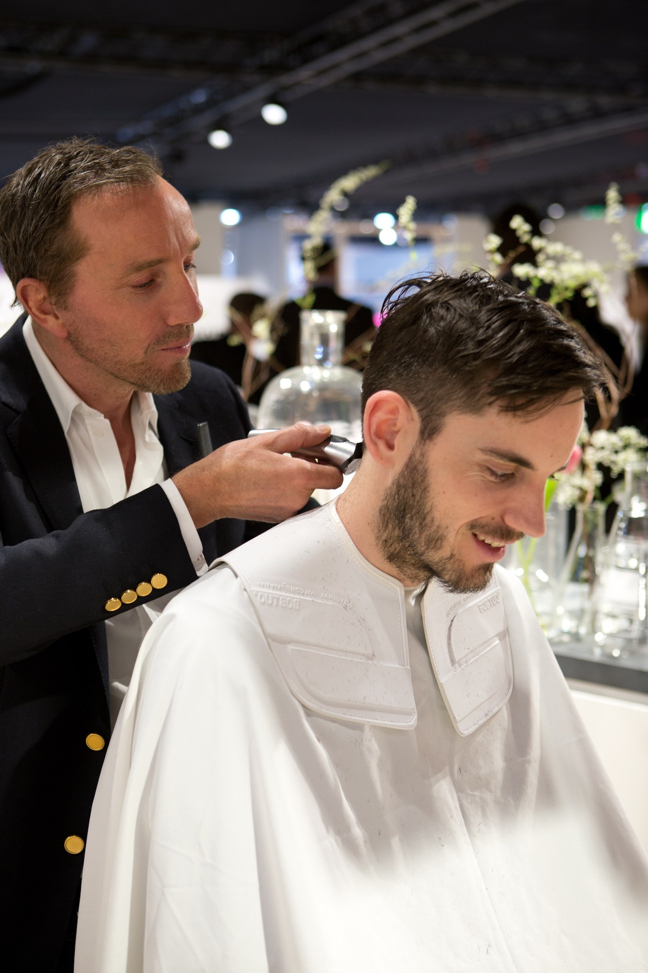 A barber in a navy blazer cuts a client's hair at the EuroShop trade fair.