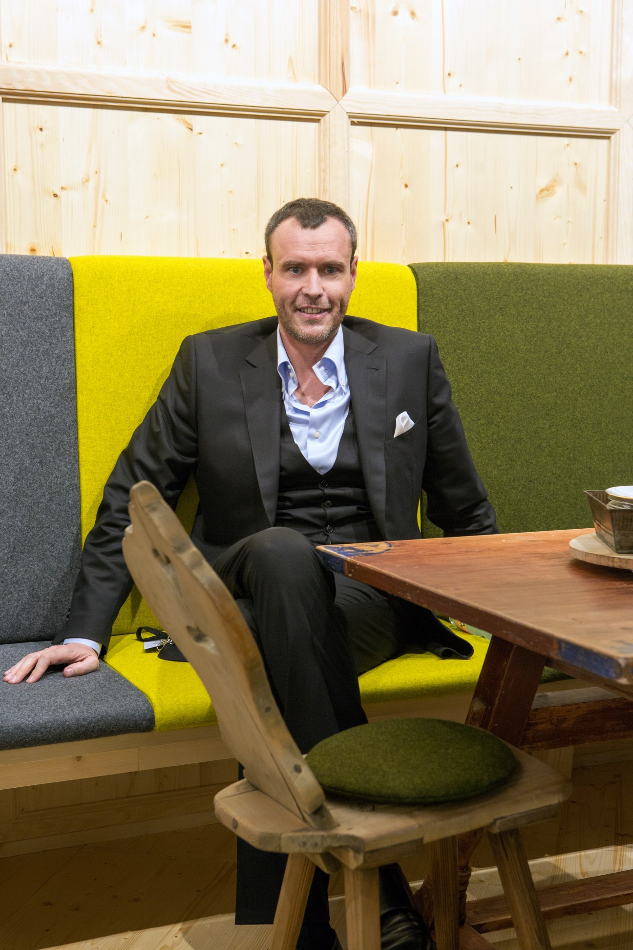Bernhard Schweitzer, CEO of Schweitzer, sits on a colorful modern sofa in a wooden interior.