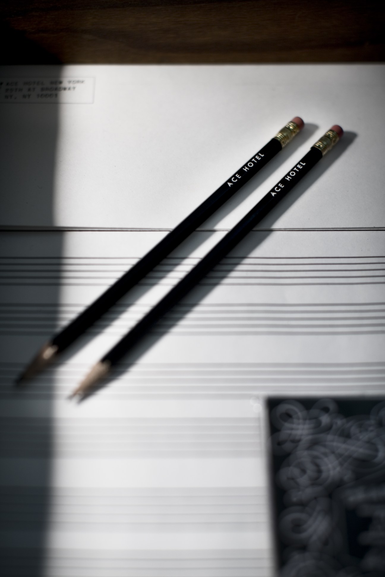 Two black pencils branded with "ACE HOTEL" text on sheet music paper.