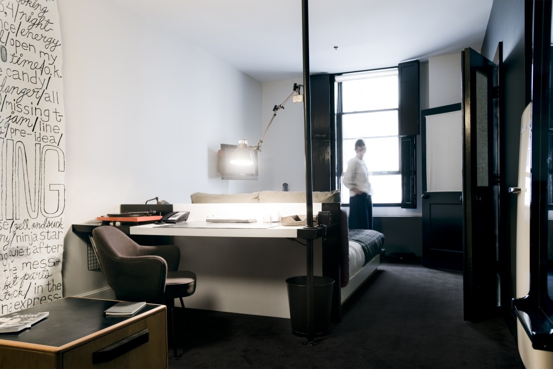 Modern hotel room at Ace Hotel New York with black window shutters, desk, chair, and bed with city views.