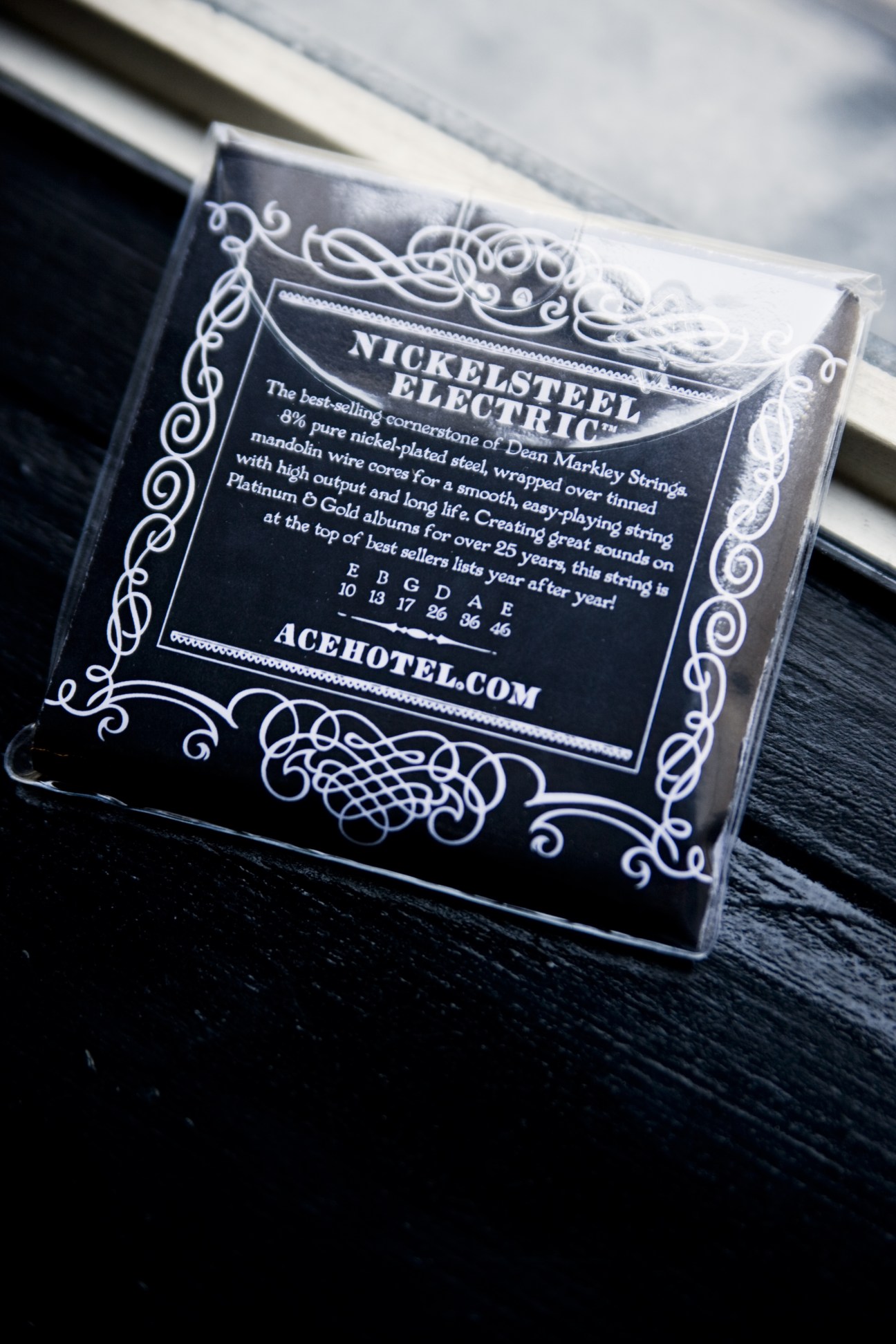 Package of Nickelsteel electric guitar strings with decorative black and white packaging on dark wood surface.